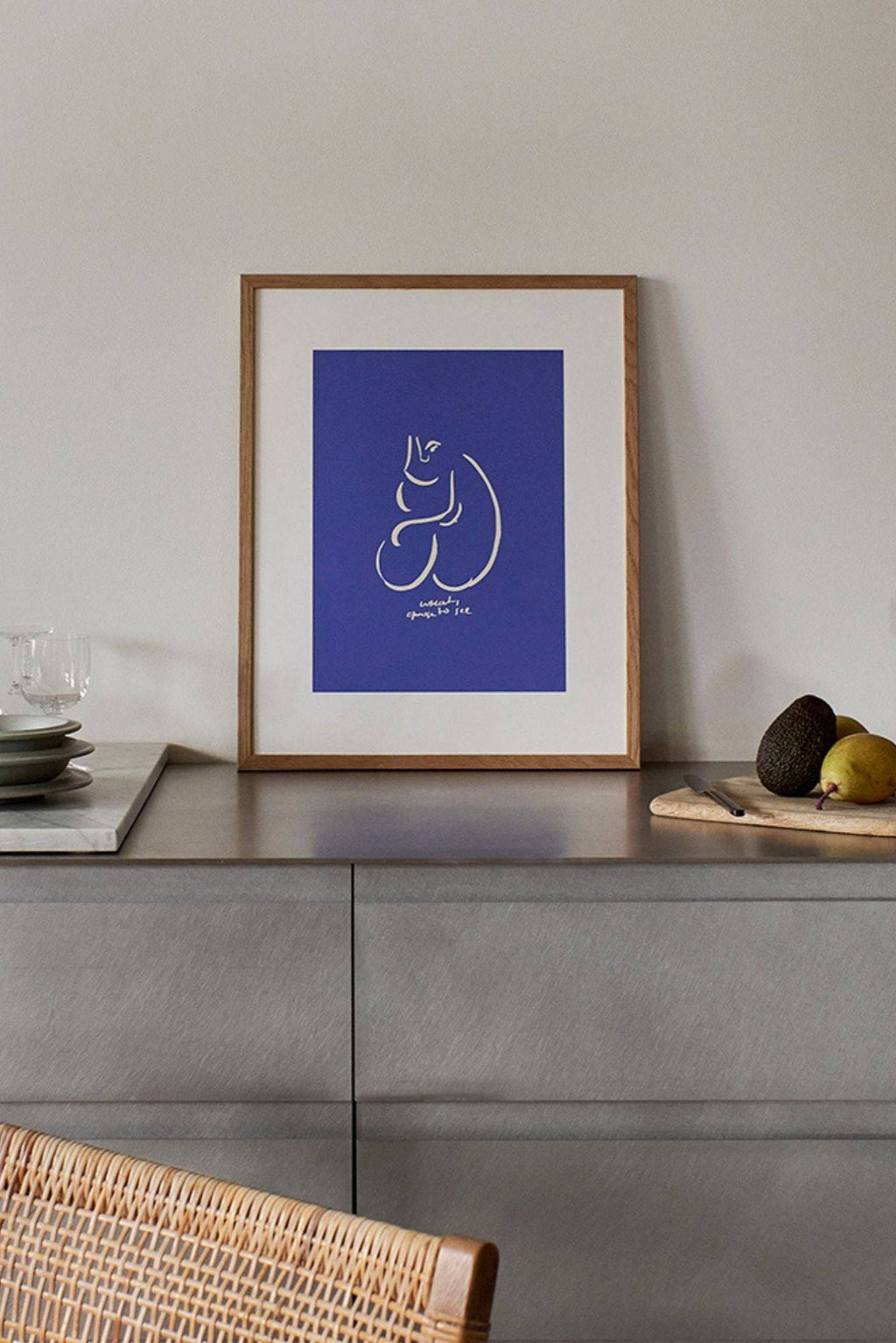 The Poster Club What I See, a modern minimalist abstract art print featuring a white continuous line drawing of a seated figure and text on a vibrant royal blue background, framed in natural oak wood with a crisp white mat. This contemporary Scandinavian-style wall art is perfect for enhancing a gallery wall in a living room, bedroom, or kitchen.