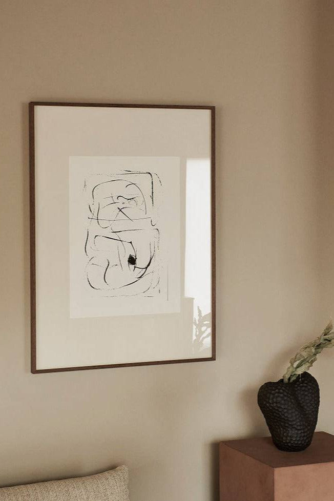 The Poster Club L' Univers, an abstract art print featuring bold, organic black line drawings on a light cream background, elegantly framed in a dark brown wood frame with a crisp white mat. This minimalist graphic art print is perfect for contemporary gallery walls, Scandinavian living rooms, or modern bedroom decor.