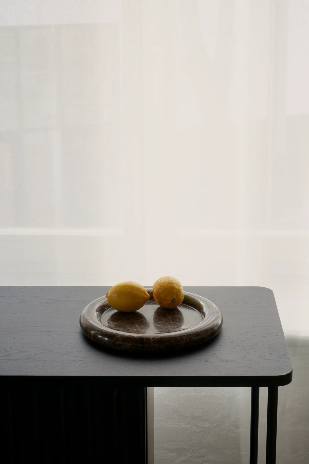 TAMO Luva Marble Tray, a round, genuine dark brown marble tray with subtle white veining, featuring two vibrant yellow lemons, styled on a dark wooden table. Ideal for sophisticated home decor.