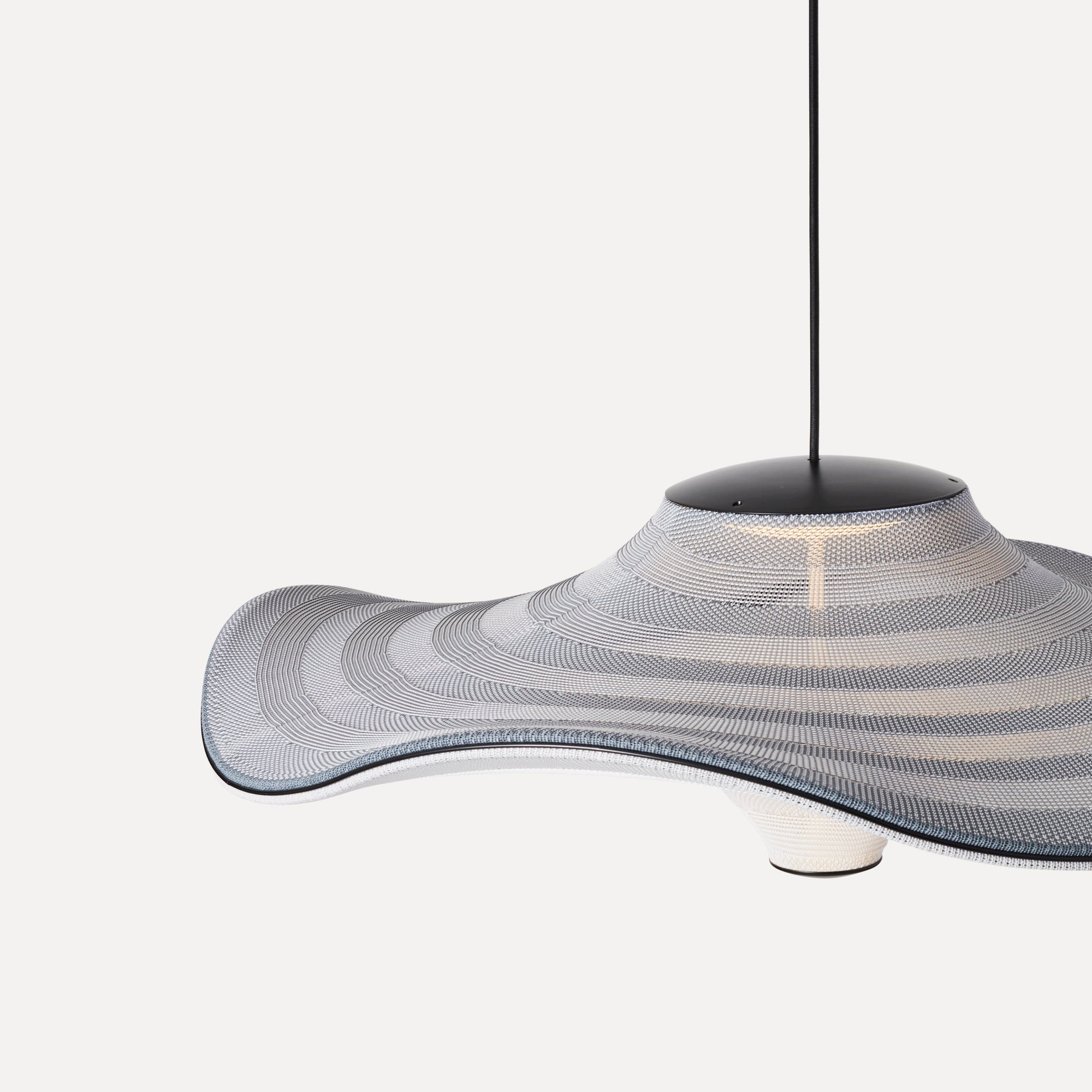 Made by Hand Flying Ø58 Pendant Lamp, a distinctive organic modern pendant lamp featuring a wide, wavy, sombrero-like shade crafted from intricately woven light grey, white, and dark grey textile with a subtle blue edge accent. Its sculptural form and textured fabric diffuse a soft, ambient light from its matte black metal top canopy and bottom ring. This contemporary ceiling light is perfect for adding a statement to Scandinavian living rooms, minimalist dining areas, or organic modern interiors.