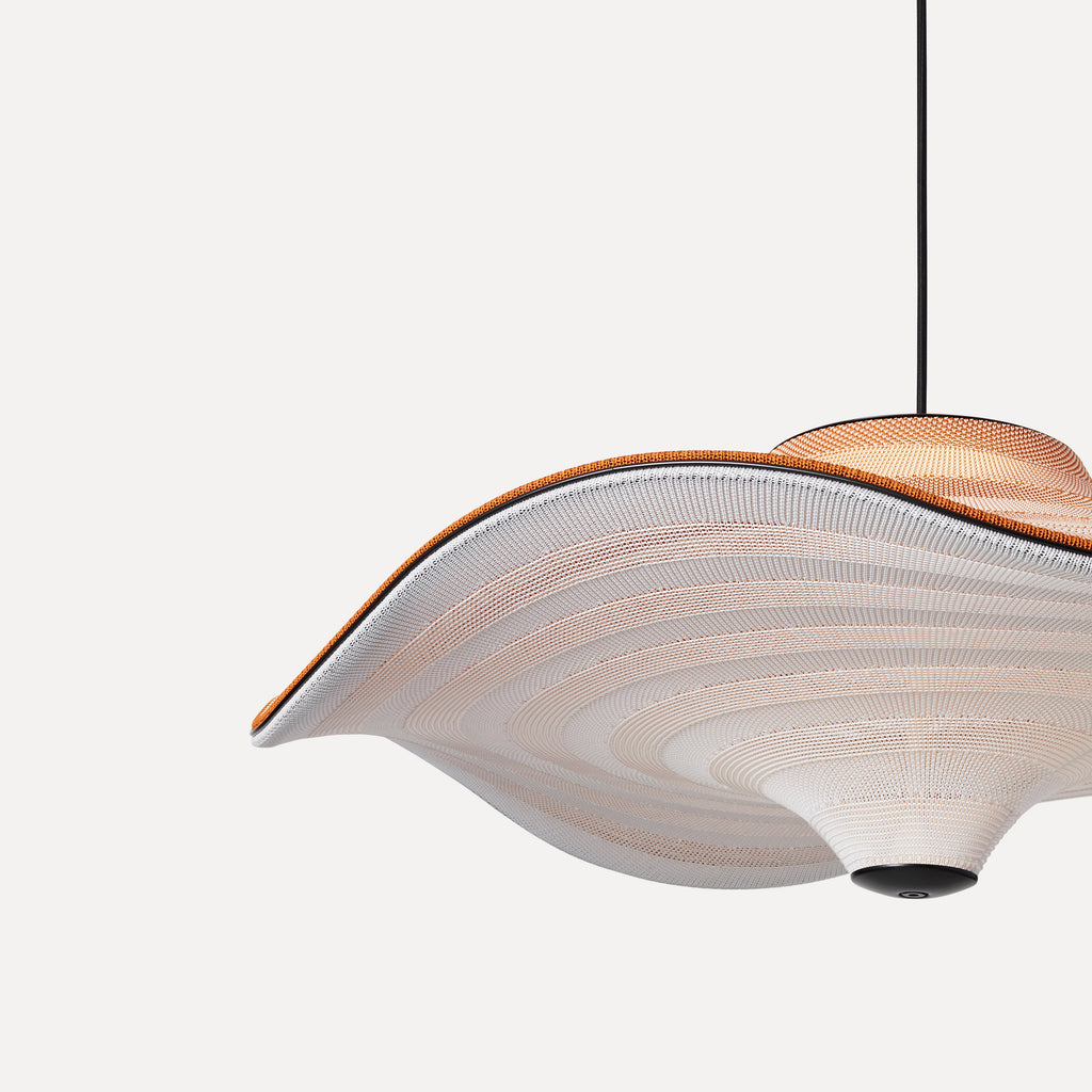 Made by Hand Flying Ø58 Pendant Lamp, an organic modern suspension light featuring a wide, undulating woven textile shade in cream and subtle terracotta orange, showcasing a delicate striped knit pattern and matte black metal details. This sculptural hanging lamp casts a soft glow, perfect for minimalist living rooms, contemporary dining areas, or design-forward bedrooms.