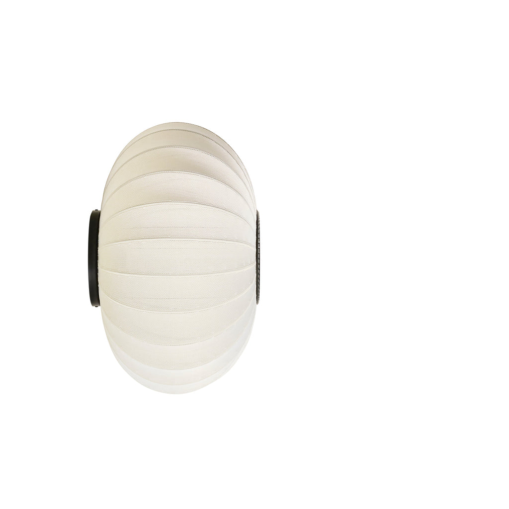 Made by Hand Knit-Wit Ø57 Oval Wall Light, a modern Scandinavian wall light featuring a warm cream-colored knitted textile shade with a distinct ribbed texture, creating a soft, inviting glow. This organic modern wall lamp is perfect for ambient lighting in a minimalist living room, cozy bedroom, or contemporary entryway.