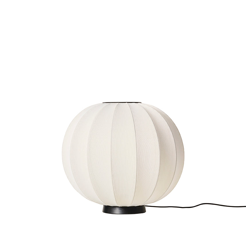 Made by Hand Knit-Wit Ø60 Floor Lamp, a contemporary globe floor lamp featuring a soft off-white knitted textile shade with a distinct ribbed texture and a minimalist matte black metal base. This organic modern lighting piece provides warm, ambient illumination. Perfect for a Scandinavian living room, cozy reading nook, or modern bedroom decor.