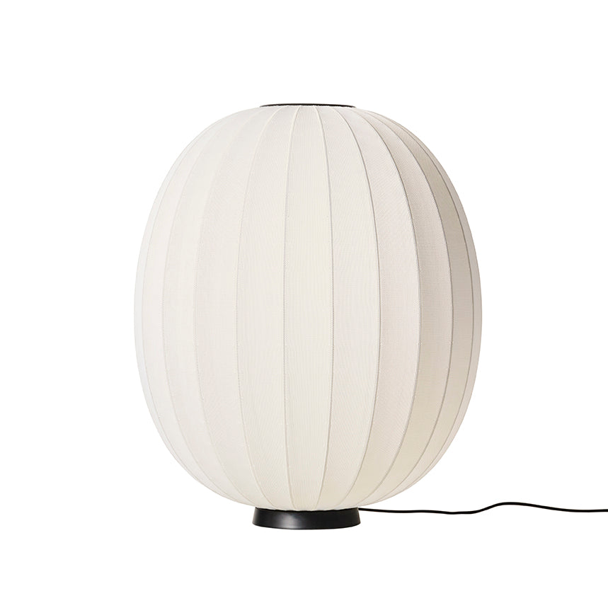 Made by Hand Knit-Wit Ø65 Floor Lamp, a contemporary oval floor lamp featuring a cream-colored knitted fabric shade with a distinctive ribbed texture and a minimalist matte black metal base. This elegant Scandinavian design offers soft, ambient lighting for modern living rooms, cozy bedrooms, or organic modern interiors.