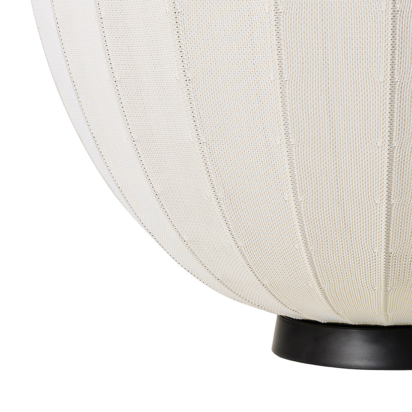 Made by Hand Knit-Wit Ø65 Floor Lamp, a large modern minimalist floor lamp with a spherical, globe-like shade crafted from a cream-colored knitted textile, featuring subtle vertical ribs and a soft, textured appearance. This Scandinavian-inspired standing lamp sits on a sleek matte black metal base, providing warm ambient light. Perfect for a cozy living room, contemporary bedroom, or organic modern lounge area.