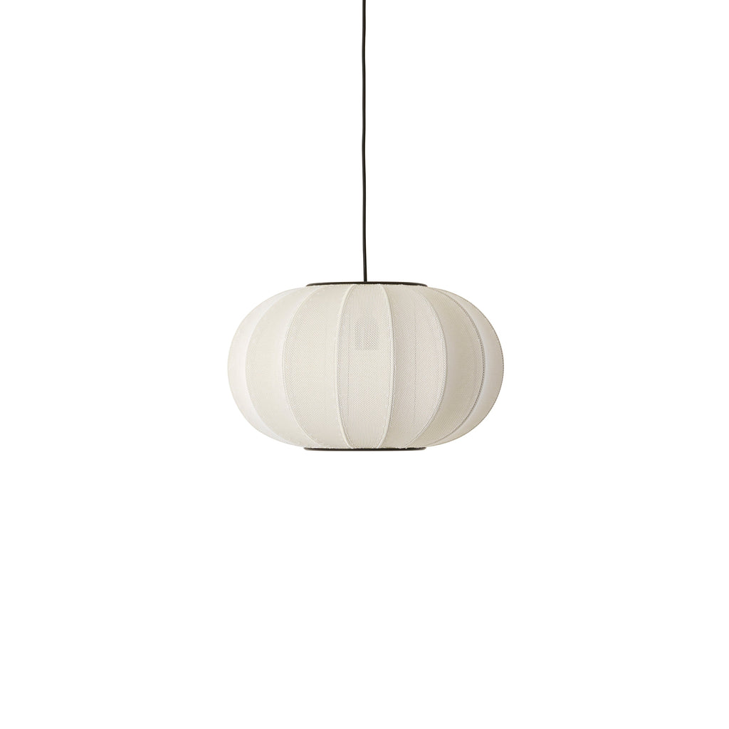 Made by Hand Knit-Wit Ø45 Oval Pendant Lamp, a Scandinavian modern ceiling light featuring a spherical, ribbed cream-colored knitted textile shade with a soft, inviting texture and a dark suspension cable. This organic modern hanging lamp provides a warm, diffused glow, ideal for cozy lighting in minimalist living rooms, bedrooms, or dining spaces.