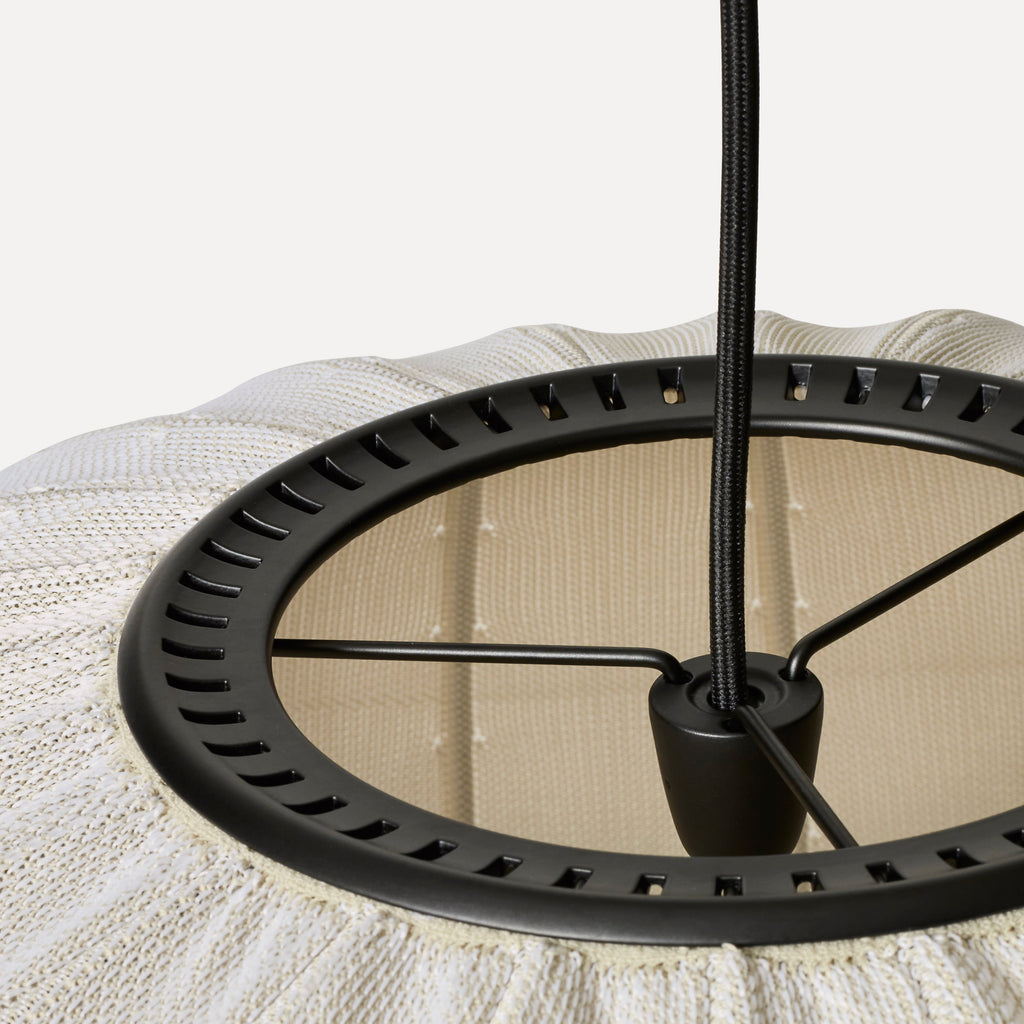 Made by Hand Knit-Wit Ø45 Oval Pendant Lamp, a contemporary ceiling light featuring a textured cream knitted fabric shade with a distinctive ribbed pattern and an underlying beige layer, supported by a sleek matte black metal frame and braided textile cable. This organic modern pendant lamp provides cozy ambient lighting, perfect for Scandinavian living rooms, minimalist bedrooms, or stylish dining areas.