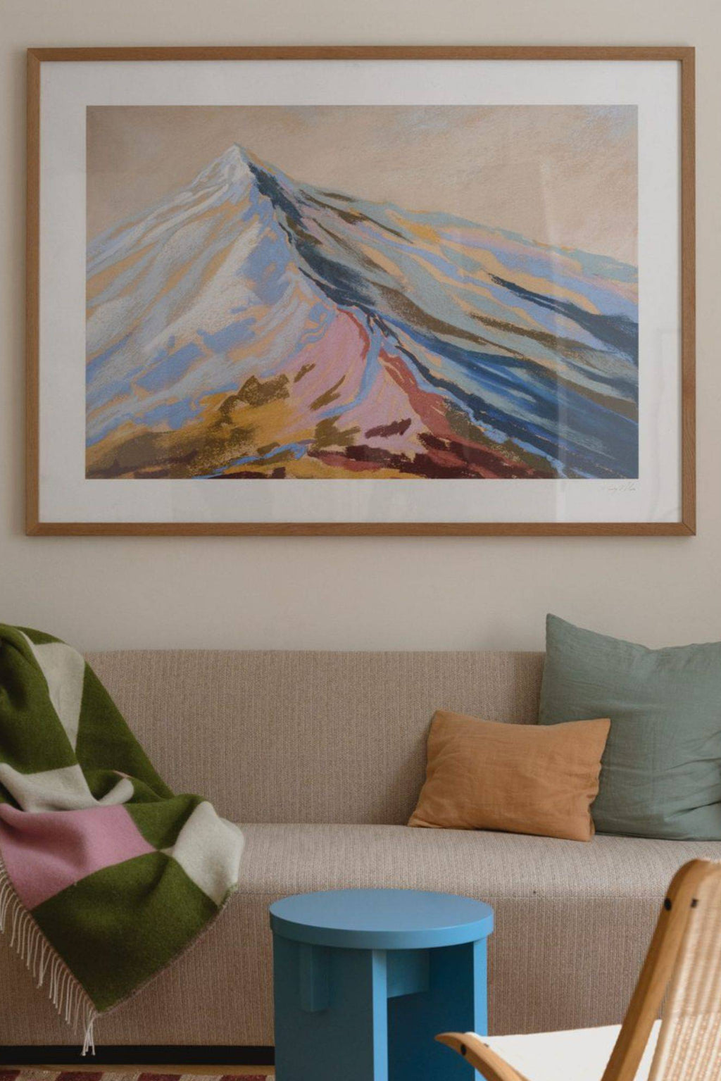 The Poster Club Velvet Peak III, an abstract landscape art print featuring a stylized mountain in soft blues, pinks, and gold tones on a subtle beige background, presented with a crisp white mat and framed in a light natural oak frame. This contemporary wall art piece is ideal for modern living rooms, Scandinavian bedrooms, or adding a colorful focal point to any gallery wall.