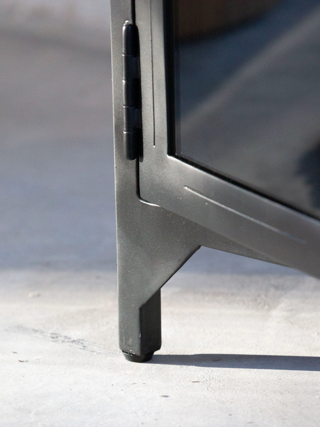 Tine K Metal High Cabinet, a sleek industrial chic storage cabinet crafted from matte black powder-coated metal with a subtly textured finish, featuring a robust hinge and angled leg detail.