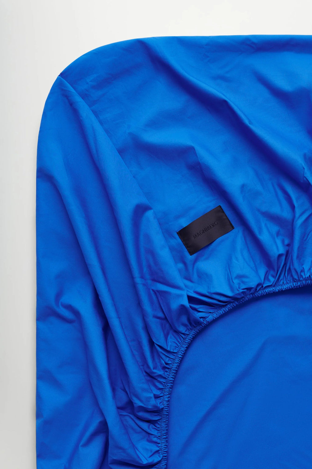 Magniberg Mother Poplin Fitted Sheet, a vibrant cobalt blue premium cotton poplin fitted sheet featuring a crisp, smooth texture and fully elasticized edges for a snug fit. This modern minimalist bedding essential offers a bold color statement for contemporary bedrooms or a luxurious sleep sanctuary.