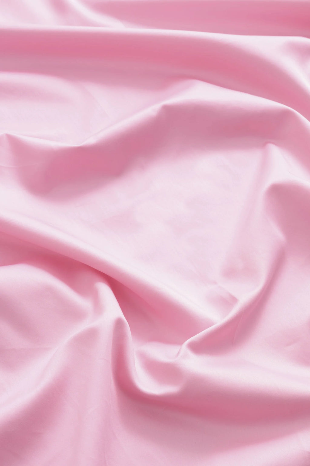 Magniberg Mother Sateen Flat Sheet, a luxurious light pink sateen flat sheet with a smooth, silky texture and a subtle lustrous sheen, showcasing elegant drapes and soft folds. This contemporary pink bed linen is perfect for creating a serene and opulent bedroom aesthetic.