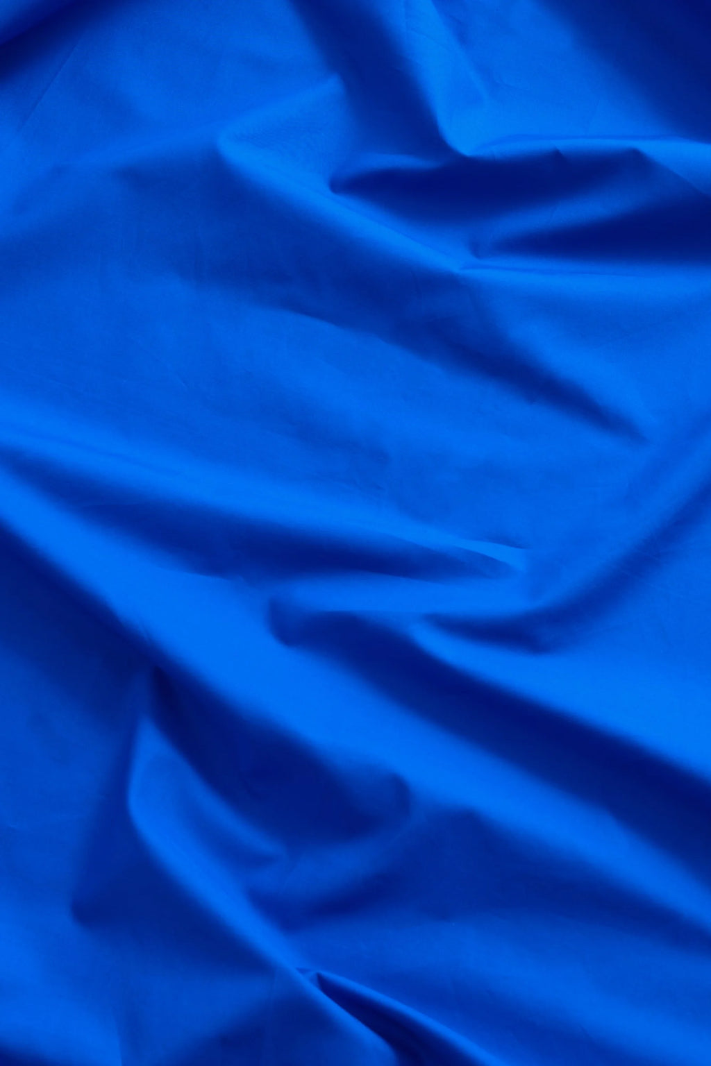 Magniberg Mother Poplin Flat Sheet, a vibrant royal blue cotton poplin flat sheet with a smooth, crisp texture and elegant, flowing folds. This premium bedding offers a bold color statement, perfect for modern minimalist or contemporary bedrooms seeking luxury cotton sheets.