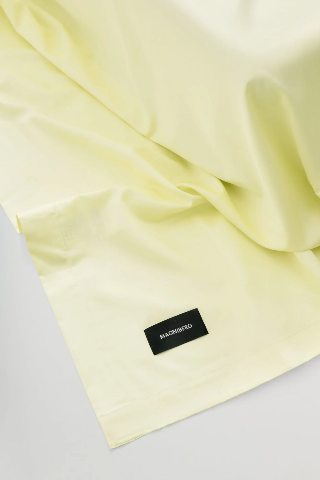 Magniberg Mother Sateen Flat Sheet, a luxurious pale yellow sateen bed sheet crafted from smooth, high-quality cotton with a subtle lustrous finish and elegant drape. This soft yellow flat sheet features a minimalist design, perfect for creating a serene and sophisticated atmosphere in modern bedrooms and contemporary interiors.