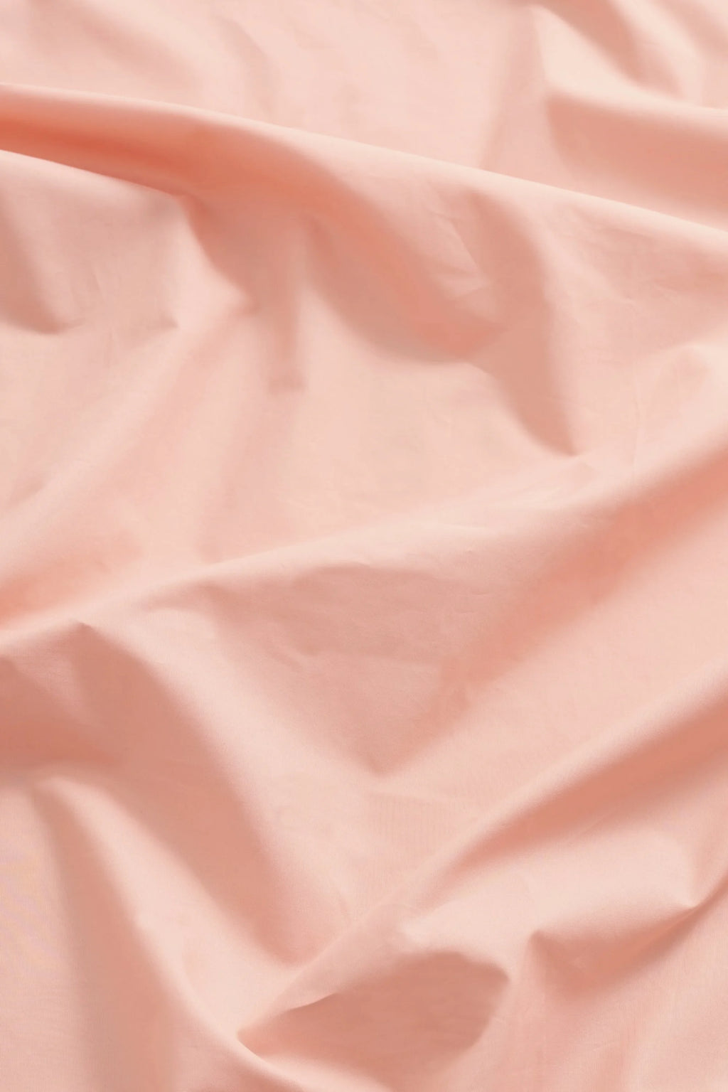 Magniberg Mother Poplin Fitted Sheet, a luxurious blush pink fitted sheet crafted from crisp cotton poplin fabric, showcasing a smooth texture with soft folds and subtle creases. This modern minimalist bedding is perfect for creating a serene and stylish sleeping space in any contemporary bedroom.
