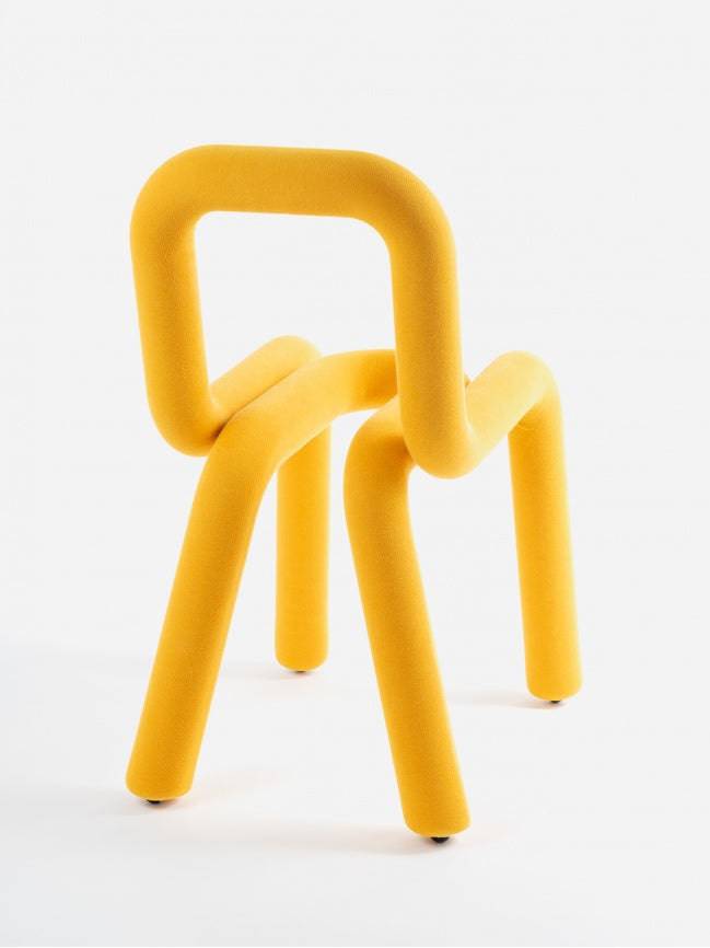 Moustache Bold Chair, a vibrant mustard yellow sculptural chair featuring a continuous, foam-padded tubular steel frame upholstered in a soft, textured fabric. Its iconic, playful design offers a bold statement piece for modern dining rooms, contemporary living spaces, or artistic office interiors.