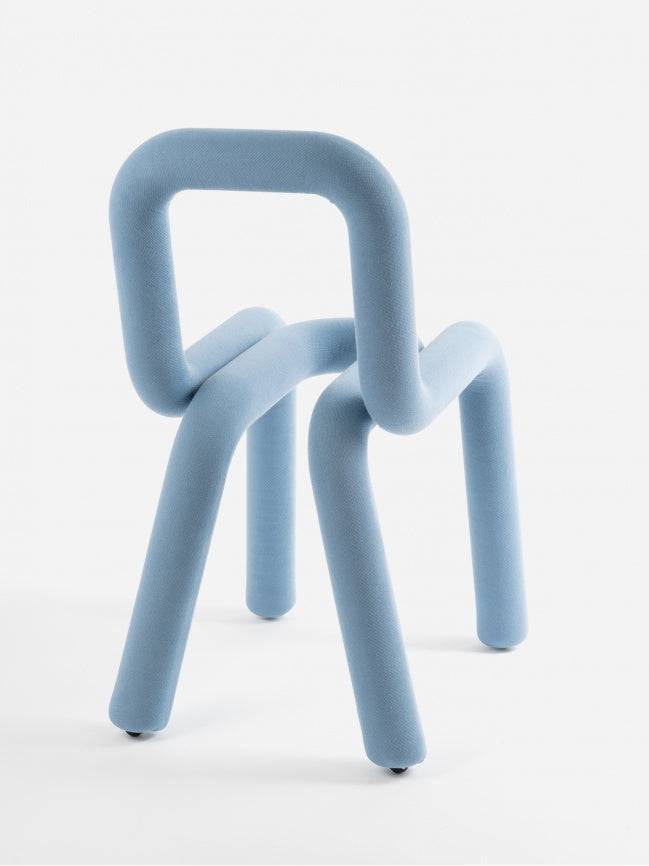 Moustache Bold Chair, a striking contemporary chair featuring a continuous, curved tubular frame entirely upholstered in a tactile, light blue fabric, creating a bold, sculptural silhouette.
