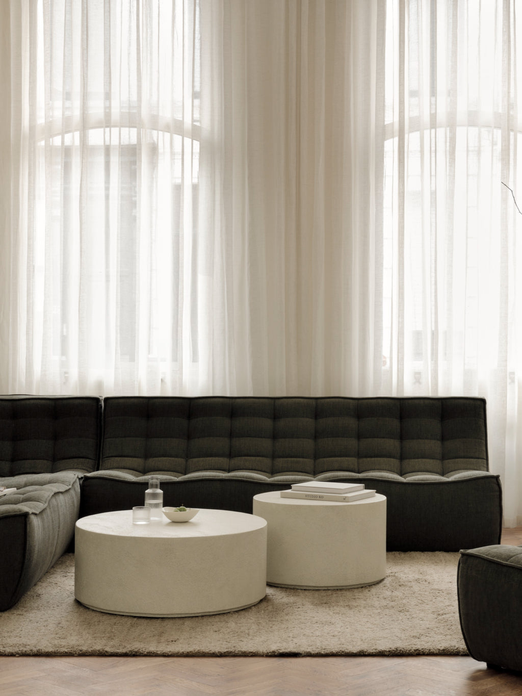 Ethnicraft Elements Coffee Table set, featuring two round microcement tables in a light cream color, placed on a textured rug in a modern living room setting.