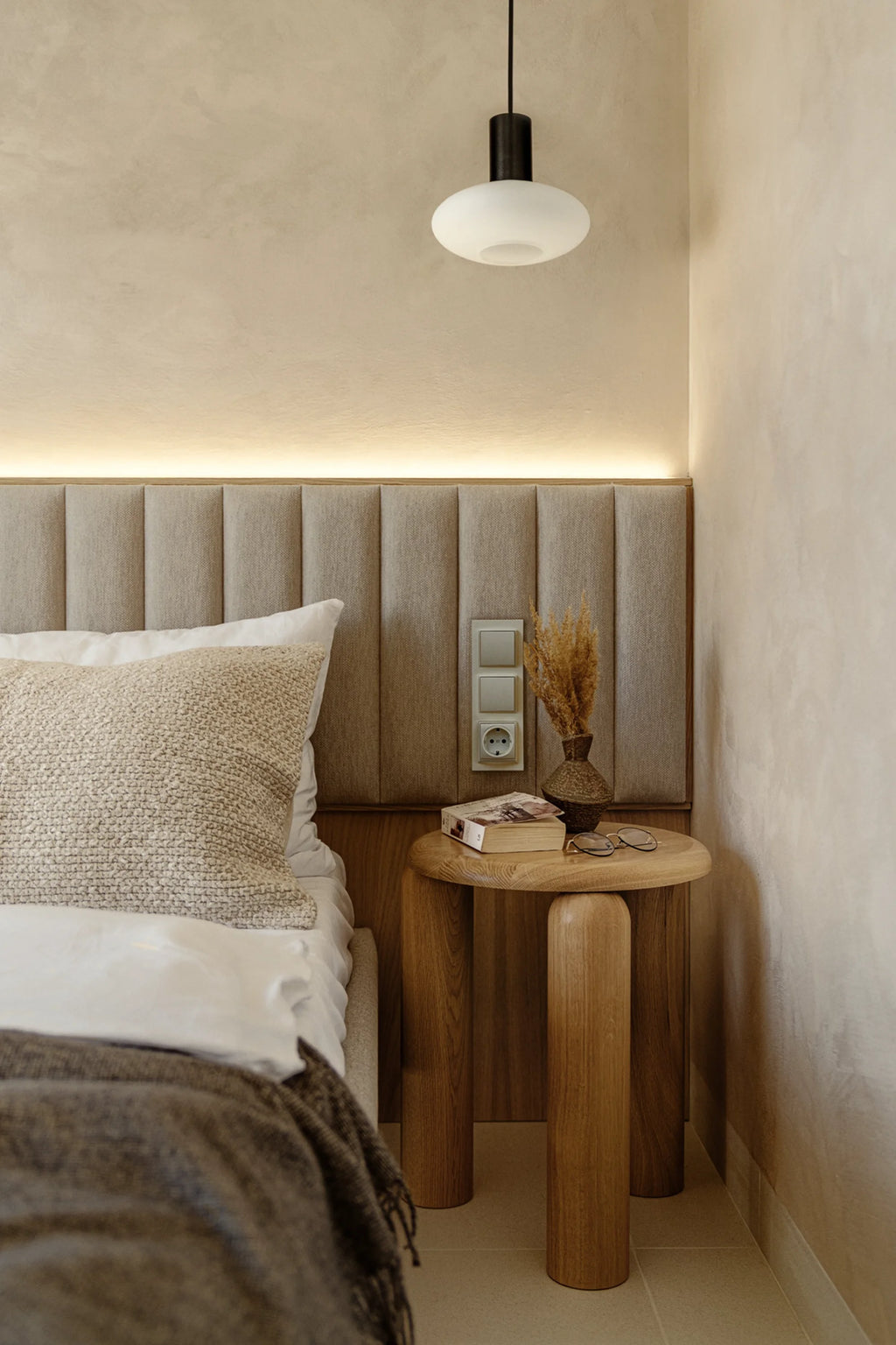 TAMO Neo Side Table in a bedroom, featuring a round, light brown oak wood top and three sturdy cylindrical legs. A premium, modern furniture piece. Ideal for a chic bedside accent.