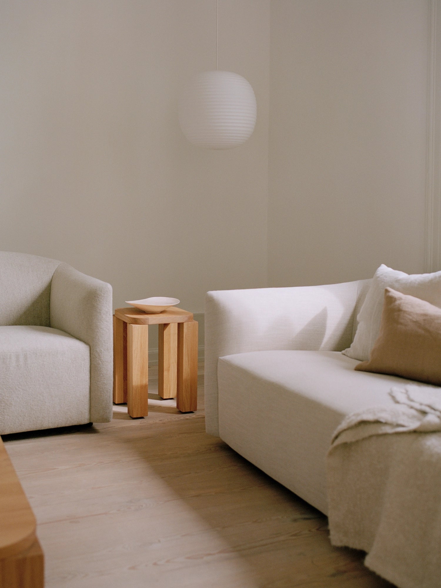 New Works Shore Sofa 3-Seater - Extended Base, presented in a light, neutral-toned fabric, alongside a matching lounge chair, creating a cohesive and elegant living room setup with a minimalist aesthetic and warm wooden accents.