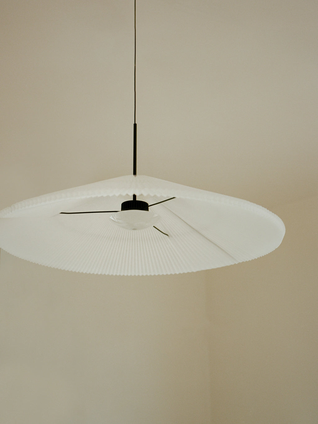 New Works Nebra Pendant Lamp, a striking white pleated textile pendant light featuring an expansive, organic-shaped shade with delicate fine pleats and a ribbed edge, anchored by sleek matte black metal hardware and a frosted glass diffuser.