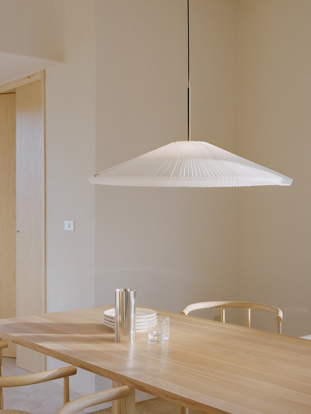 New Works Nebra Pendant Lamp, a modern minimalist ceiling light featuring a wide, translucent white finely pleated shade with a delicate ribbed edge, creating a soft, diffused glow. This contemporary Scandinavian pendant lamp is perfect for illuminating dining tables or adding organic modern style to living rooms and entryways.