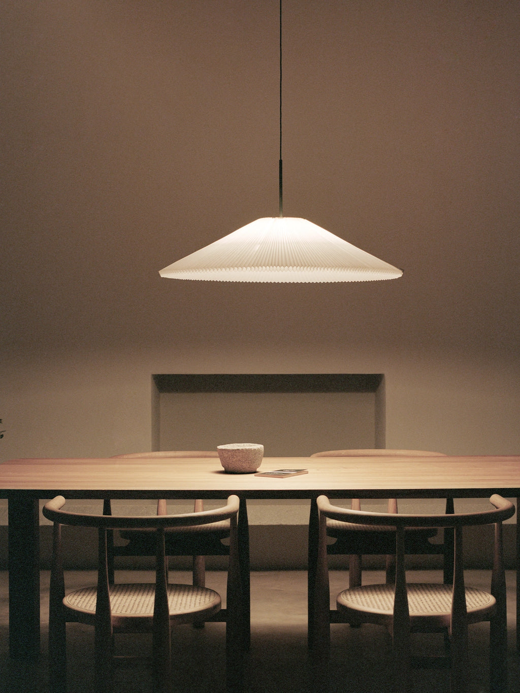 New Works Nebra Pendant Lamp, a minimalist Scandinavian ceiling light featuring a wide, shallow, white pleated shade with a distinctive ribbed texture, suspended by a slender dark cord. This contemporary pendant lamp provides soft, diffused illumination, perfect for elegant dining rooms, Japandi-style living spaces, or modern minimalist interiors.