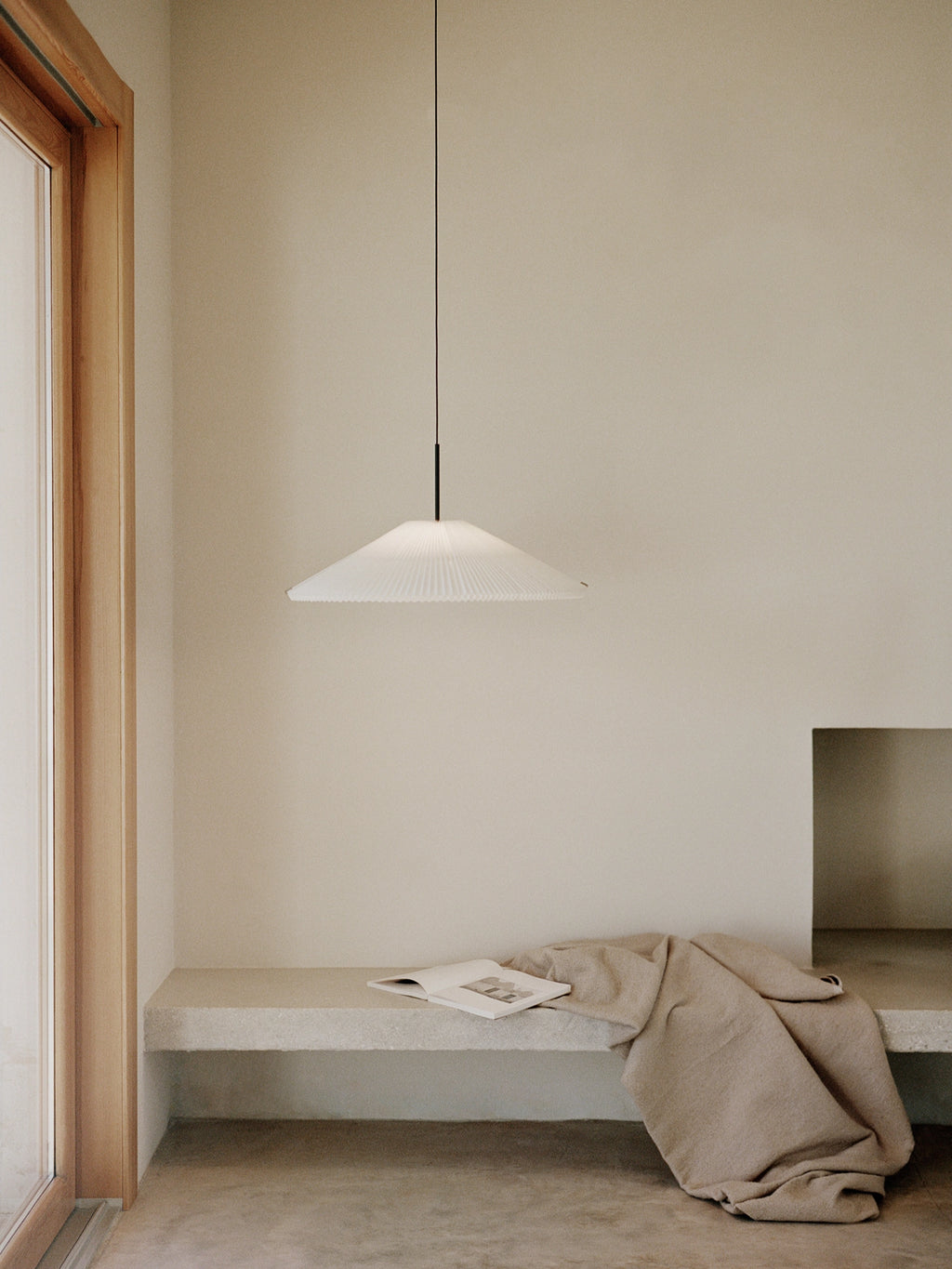 New Works Nebra Pendant Lamp, a modern minimalist pendant lamp featuring a wide, flattened conical shade crafted from delicately pleated white material, suspended by a sleek matte black rod. Its ribbed texture and clean lines evoke a Scandinavian or Japandi aesthetic, perfect for contemporary dining rooms, minimalist living areas, or serene bedroom lighting.