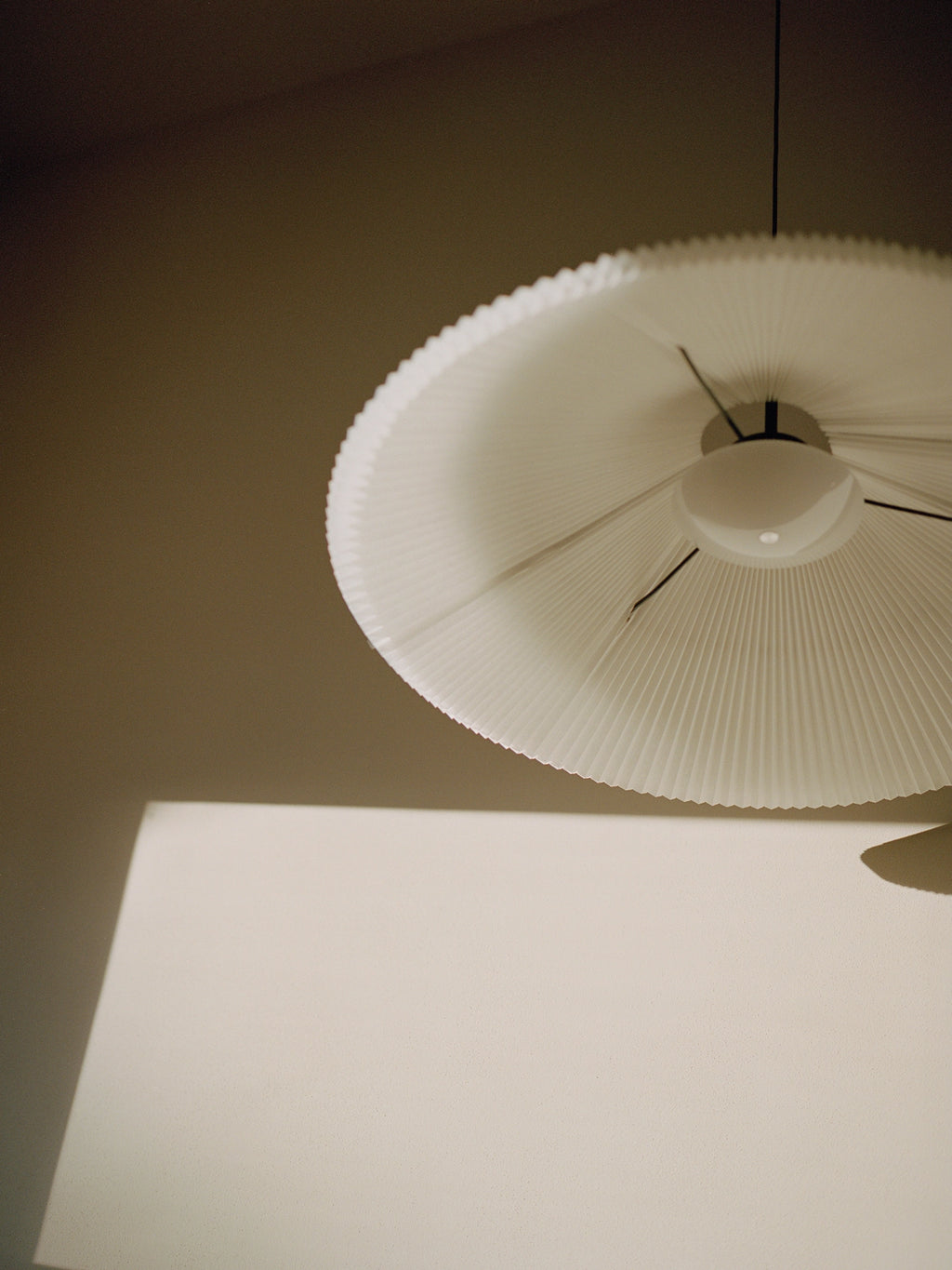 New Works Nebra Pendant Lamp, an off-white pleated fabric pendant light featuring a wide, flat disc-shaped shade with a fine fluted texture and a gently scalloped rim.