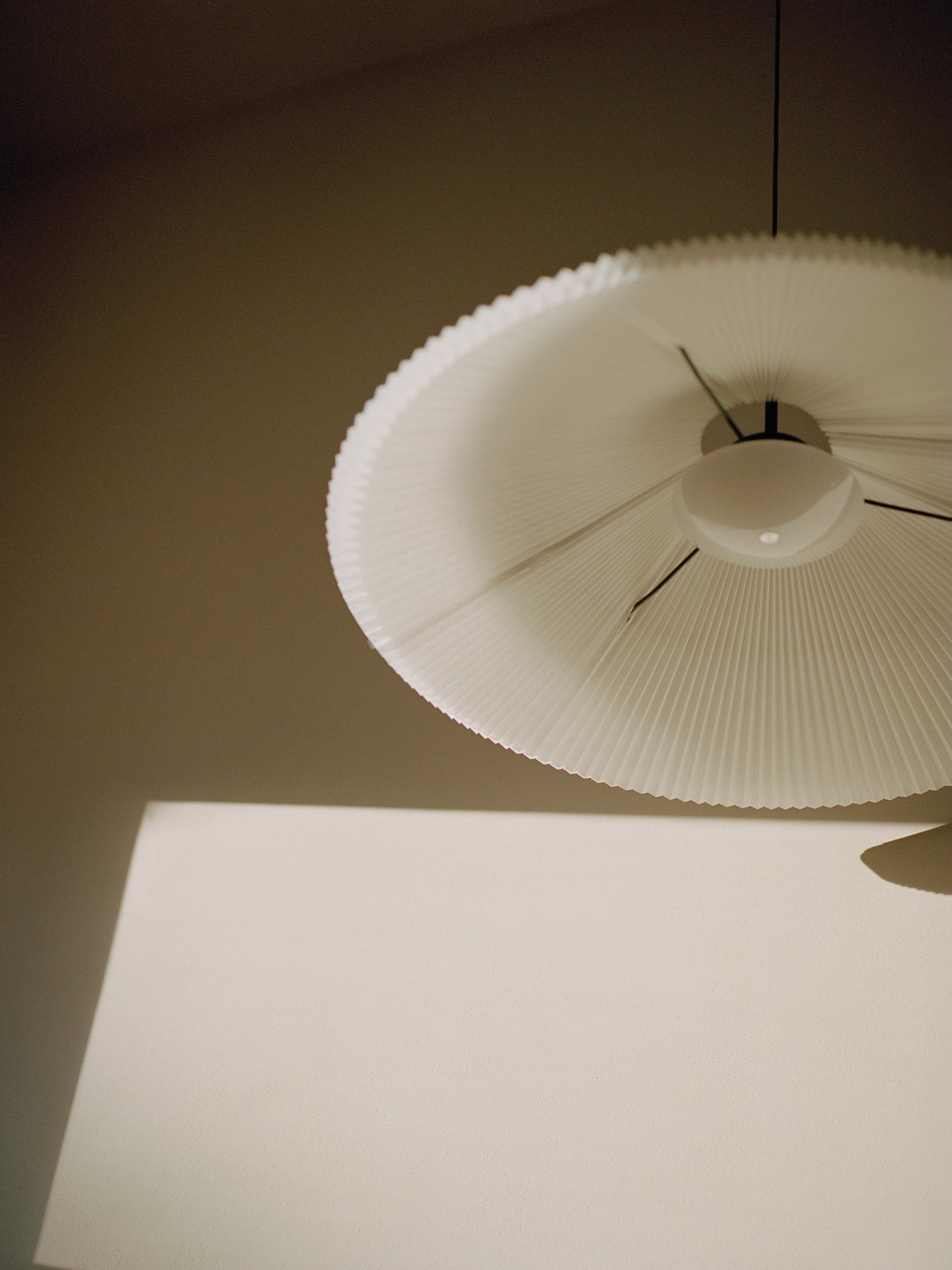 New Works Nebra Pendant Lamp, an off-white pleated fabric pendant light featuring a wide, flat disc-shaped shade with a fine fluted texture and a gently scalloped rim.