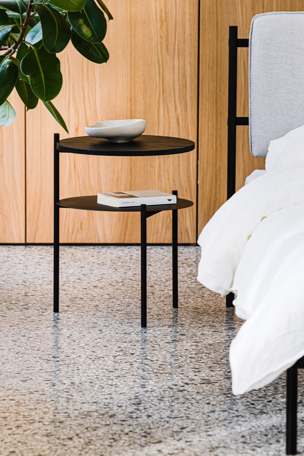 noo.ma Tu Bedside Table, a modern minimalist two-tier side table crafted from sleek matte black metal, featuring two round shelves and slender cylindrical legs that create a clean, contemporary profile. This versatile black nightstand is ideal for compact Scandinavian bedrooms, industrial chic living rooms, or as a functional accent in modern homes.