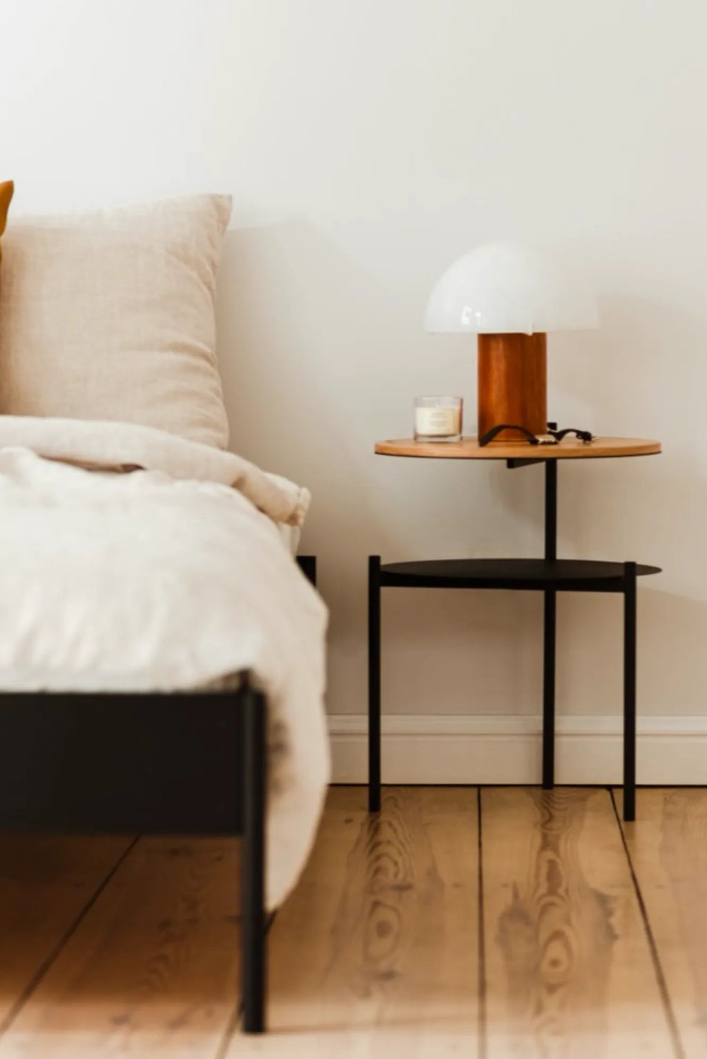 noo.ma Tu Bedside Table, a sleek modern minimalist bedside table featuring a matte black metal frame with two distinct round shelves. The upper shelf is crafted from natural light wood, providing a warm contrast to the lower matte black metal shelf and slender support structure. Ideal as a contemporary nightstand or small side table for Scandinavian or industrial chic bedroom and living room interiors.