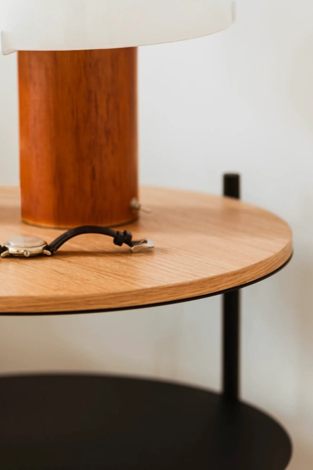 noo.ma Tu Bedside Table, a modern minimalist side table featuring a round natural light oak wood top shelf with a contrasting matte black edge, supported by sleek black metal legs. Its lower shelf is also round and crafted from matte black metal, offering practical storage and a clean silhouette. Ideal as a Scandinavian bedside table or contemporary end table for living rooms, complementing modern Nordic-inspired spaces.