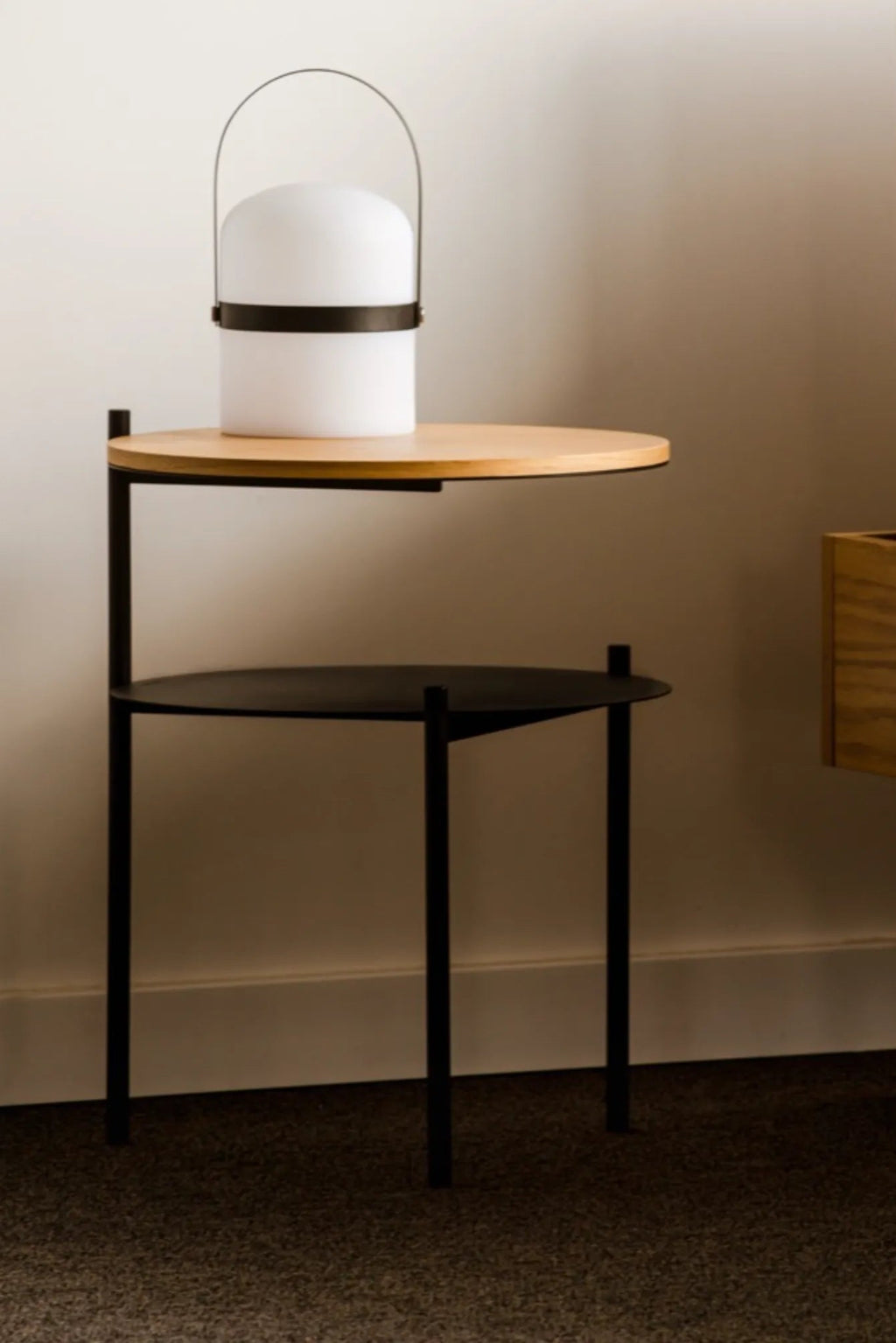noo.ma Tu Bedside Table, a modern minimalist side table featuring a matte black metal frame with sleek cylindrical legs and two round shelves. The top shelf is crafted from light natural wood, while the lower shelf is a matching matte black metal. Ideal as a Scandinavian bedside table or contemporary accent table for small living rooms.