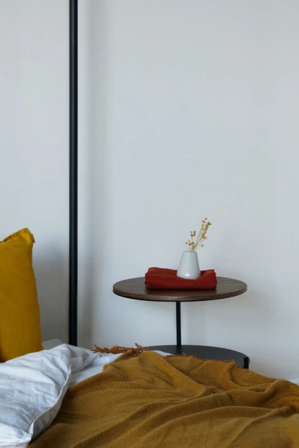 noo.ma Tu Bedside Table, a modern minimalist side table featuring a smooth dark wood round tabletop and a sleek matte black metal cylindrical stem with a matching round base. This contemporary Scandinavian accent table is perfect for bedroom bedside use or as a small living room side table.