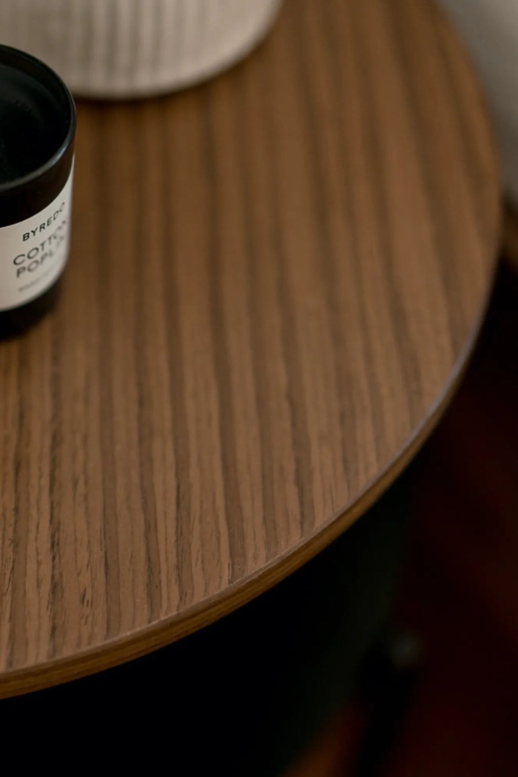 noo.ma Tu Bedside Table, a round solid wood bedside table featuring a smooth, warm brown oak wood grain top with subtle vertical patterning and a clean, minimalist profile. This modern Scandinavian side table offers timeless style, perfect as a functional bedroom accent or contemporary living room end table.