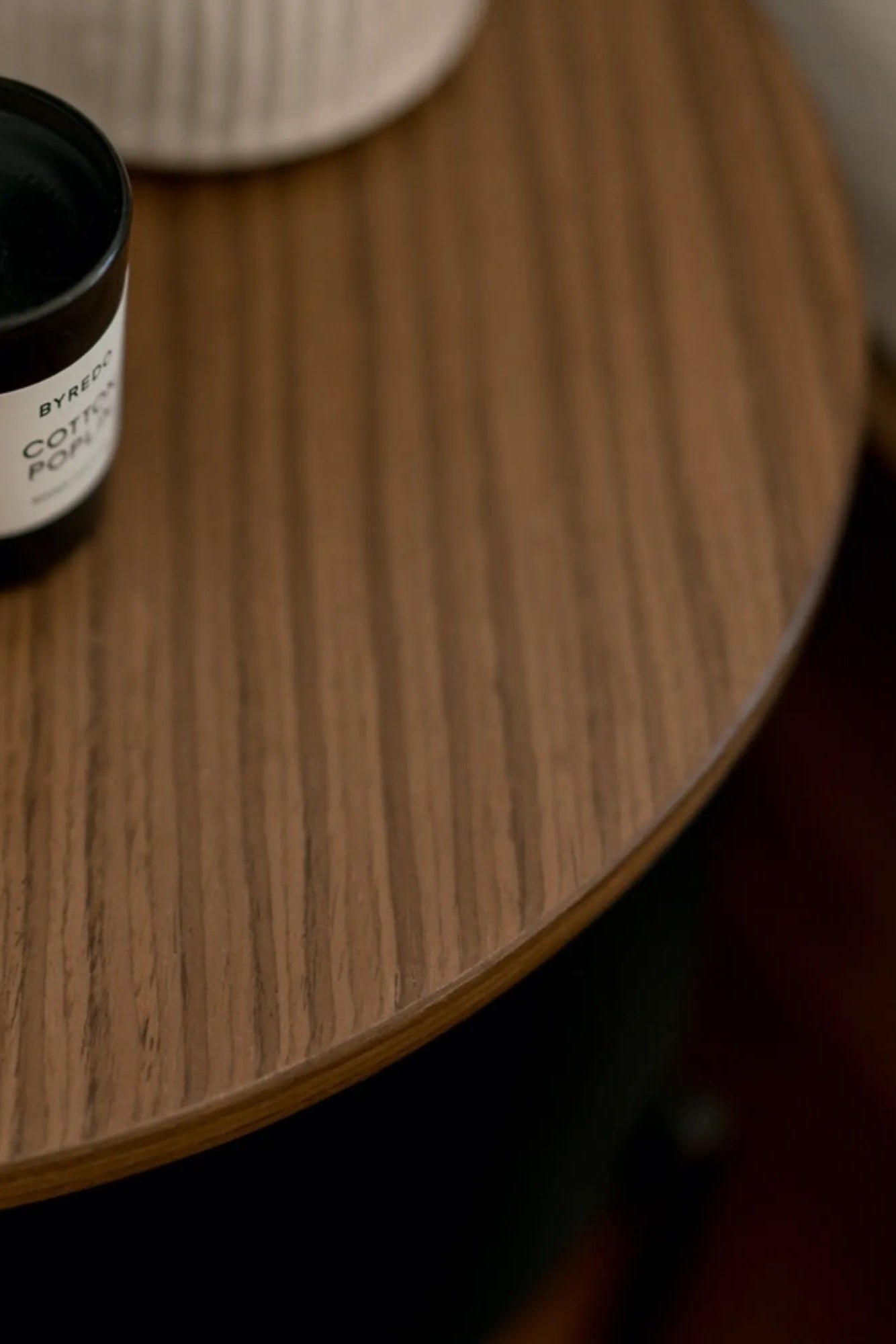 noo.ma Tu Bedside Table, a round solid wood bedside table featuring a smooth, warm brown oak wood grain top with subtle vertical patterning and a clean, minimalist profile. This modern Scandinavian side table offers timeless style, perfect as a functional bedroom accent or contemporary living room end table.