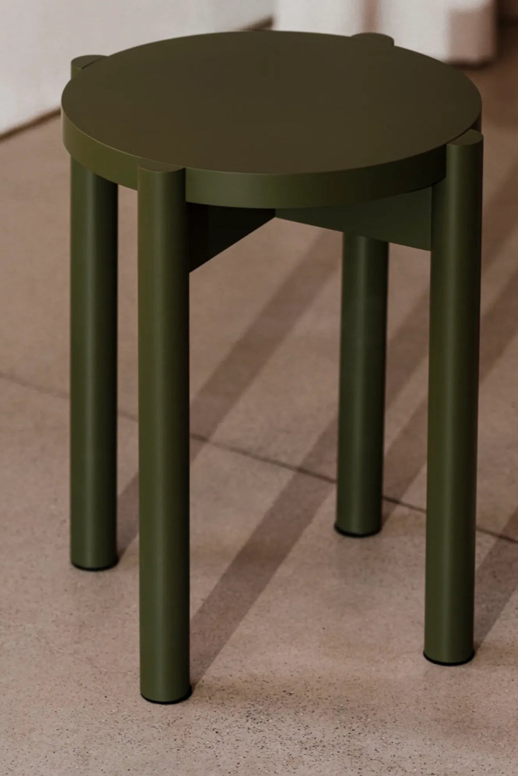 noo.ma Hopp Stool, a modern minimalist round stool crafted from durable matte olive green metal with a smooth finish and four sturdy cylindrical legs. This contemporary dark green accent stool features a clean, simple design ideal for versatile use. Perfect as a stylish side table, bedside table, or entryway stool in Scandinavian or industrial chic interiors.