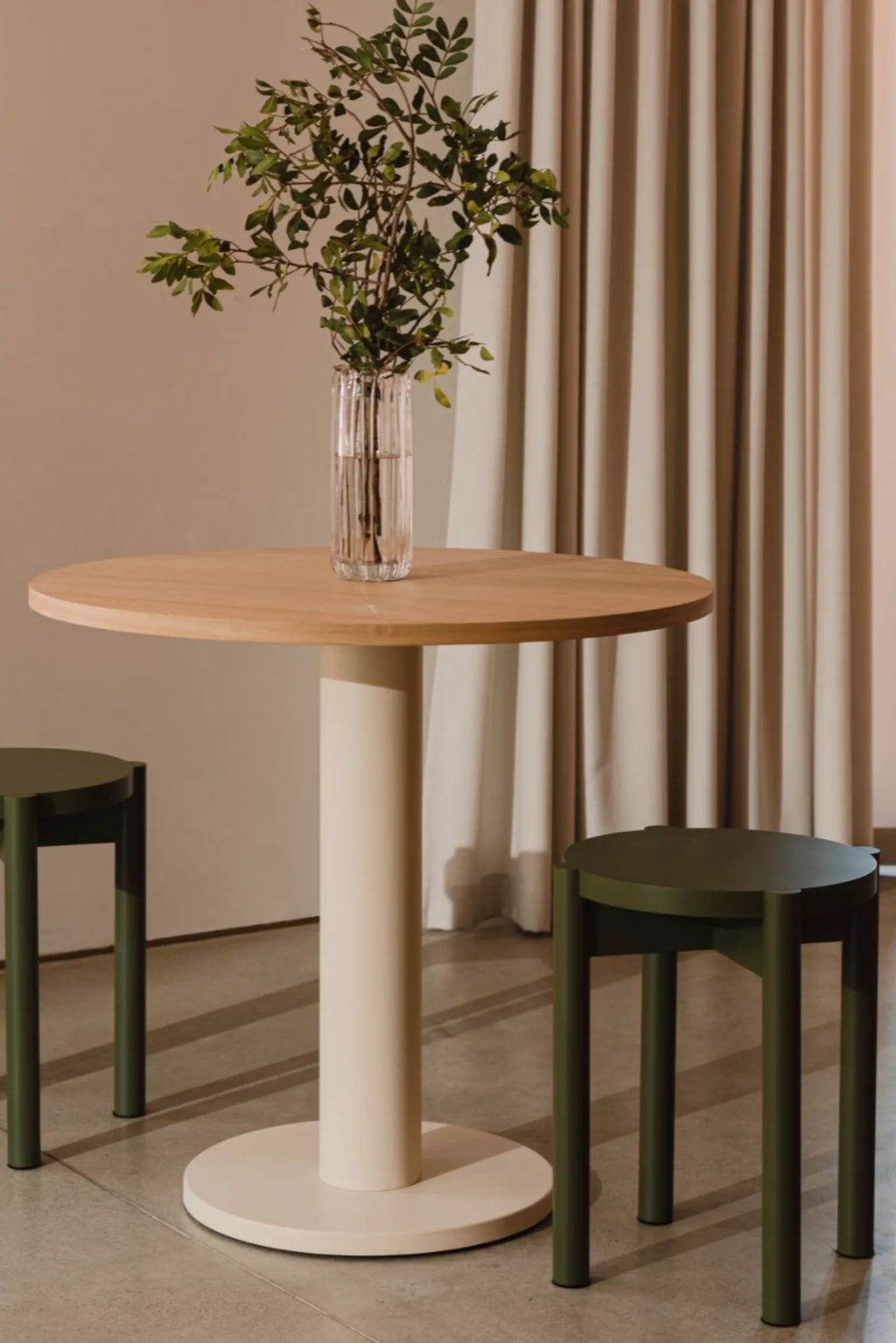 noo.ma Hopp Stool, a modern minimalist stool featuring a round seat and four sturdy cylindrical legs, crafted from matte dark olive green powder-coated metal with a clean, contemporary design. This versatile accent stool or side table is perfect for Scandinavian living rooms, Japandi bedrooms, or compact entryway spaces.