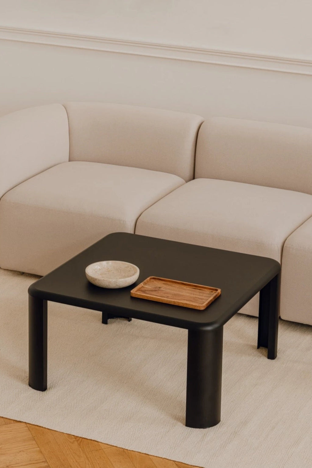 noo.ma Fli Coffee Table, a minimalist contemporary coffee table featuring a square top with gently rounded corners and a sleek matte black ash veneer finish. It stands on sculptural chunky legs, combining two cylindrical and two flat rectangular supports, creating a unique organic modern design. This stylish black coffee table is perfect for modern living rooms, minimalist interiors, or as a central piece in a contemporary lounge space.