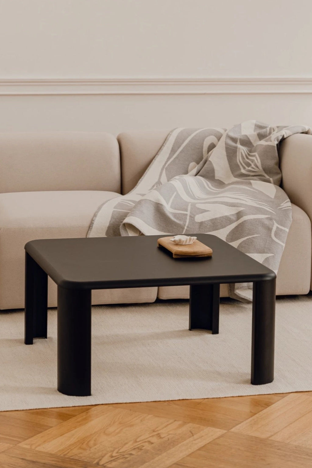 noo.ma Fli Coffee Table, a sleek matte black minimalist coffee table featuring a square tabletop with gently rounded corners and thick, cylindrical legs for a soft, contemporary silhouette. This modern accent table is perfect for minimalist living rooms or as a stylish focal point in organic modern interiors.