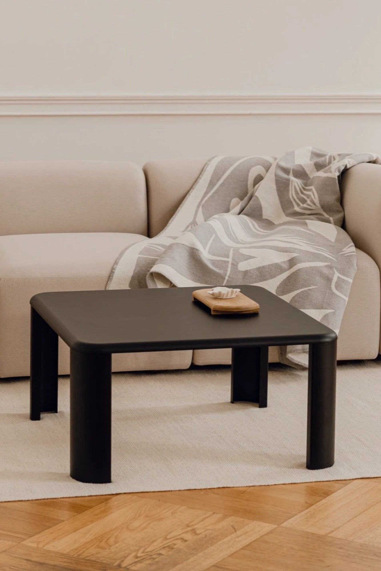 noo.ma Fli Coffee Table, a sleek matte black minimalist coffee table featuring a square tabletop with gently rounded corners and thick, cylindrical legs for a soft, contemporary silhouette. This modern accent table is perfect for minimalist living rooms or as a stylish focal point in organic modern interiors.