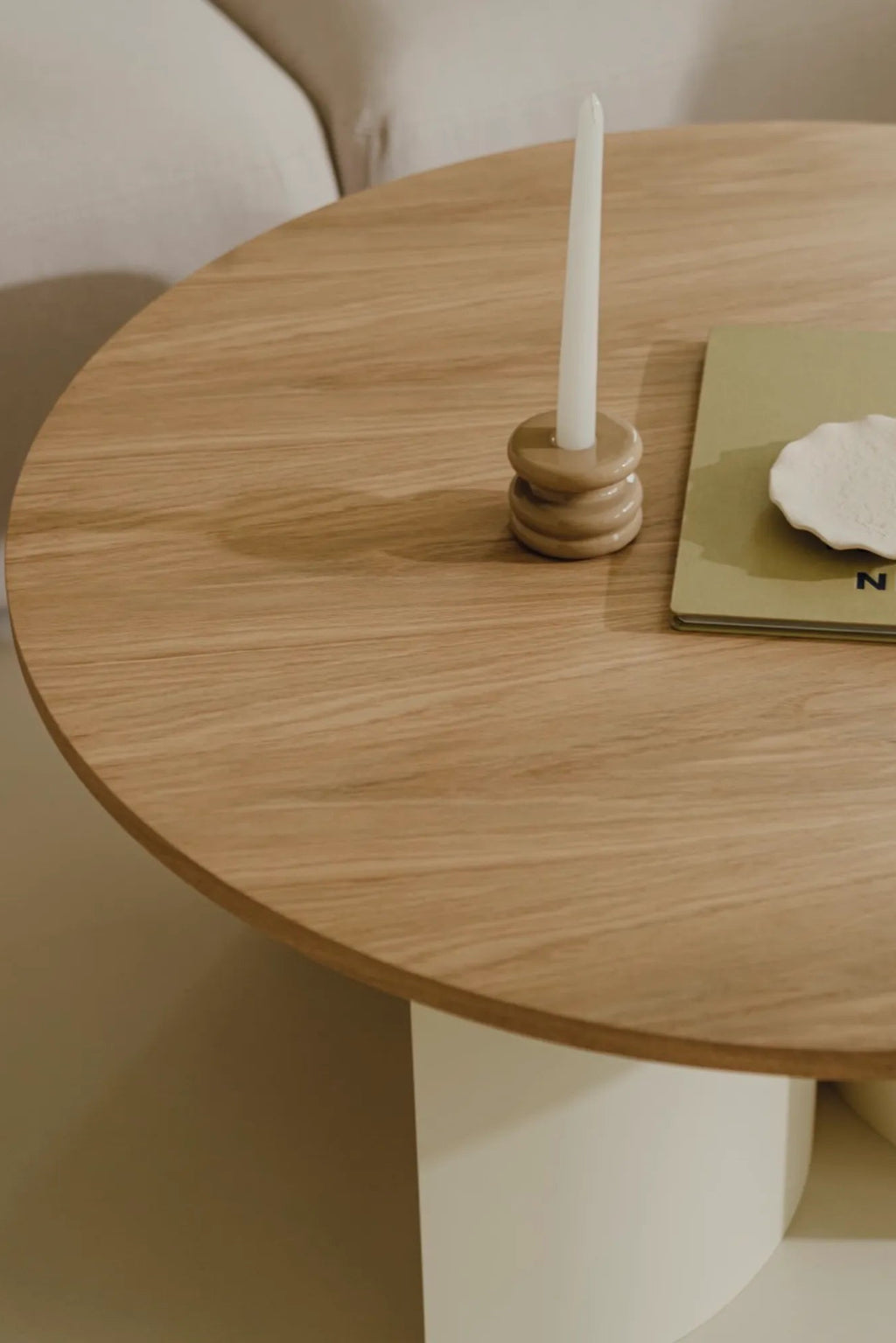 noo.ma Gavo Coffee Table, a contemporary round coffee table featuring a smooth natural solid oak tabletop with visible wood grain. It rests on a unique sculptural matte white base, embodying a minimalist and organic modern design aesthetic. Perfect for Scandinavian living rooms or modern minimalist spaces seeking a functional yet artistic centerpiece.