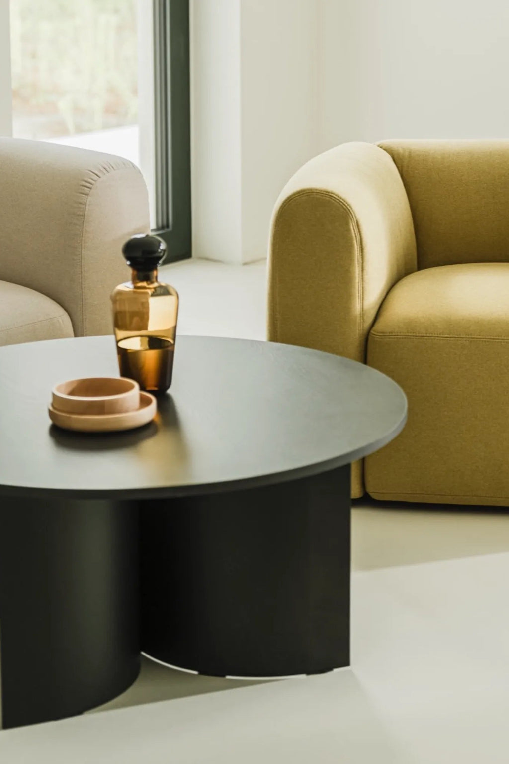 noo.ma Gavo Coffee Table, a modern minimalist round coffee table featuring a sleek matte black finish. Crafted from durable wood or MDF, its smooth dark surface complements its unique sculptural base formed by.