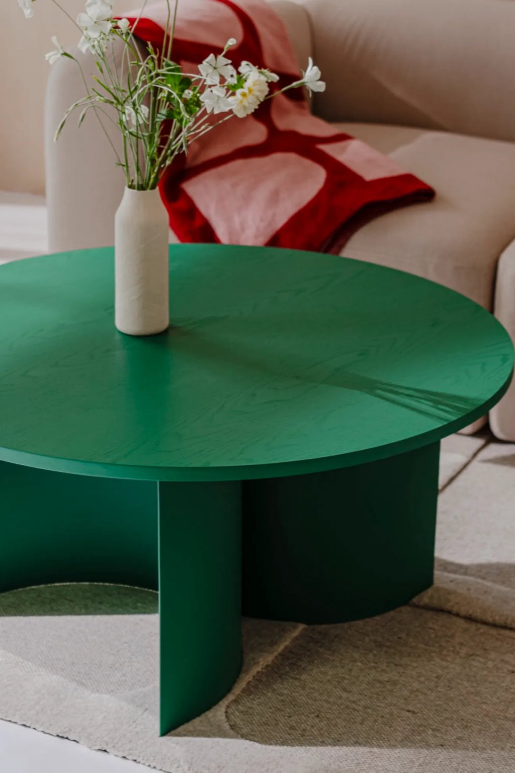 noo.ma Gavo Coffee Table, a vibrant deep emerald green round coffee table crafted from oak veneer with a smooth, matte finish that highlights the subtle wood grain. Its contemporary sculptural design features a sleek circular tabletop supported by a unique curved panel base. This modern minimalist coffee table is perfect for adding a pop of color to any living room or contemporary lounge space.