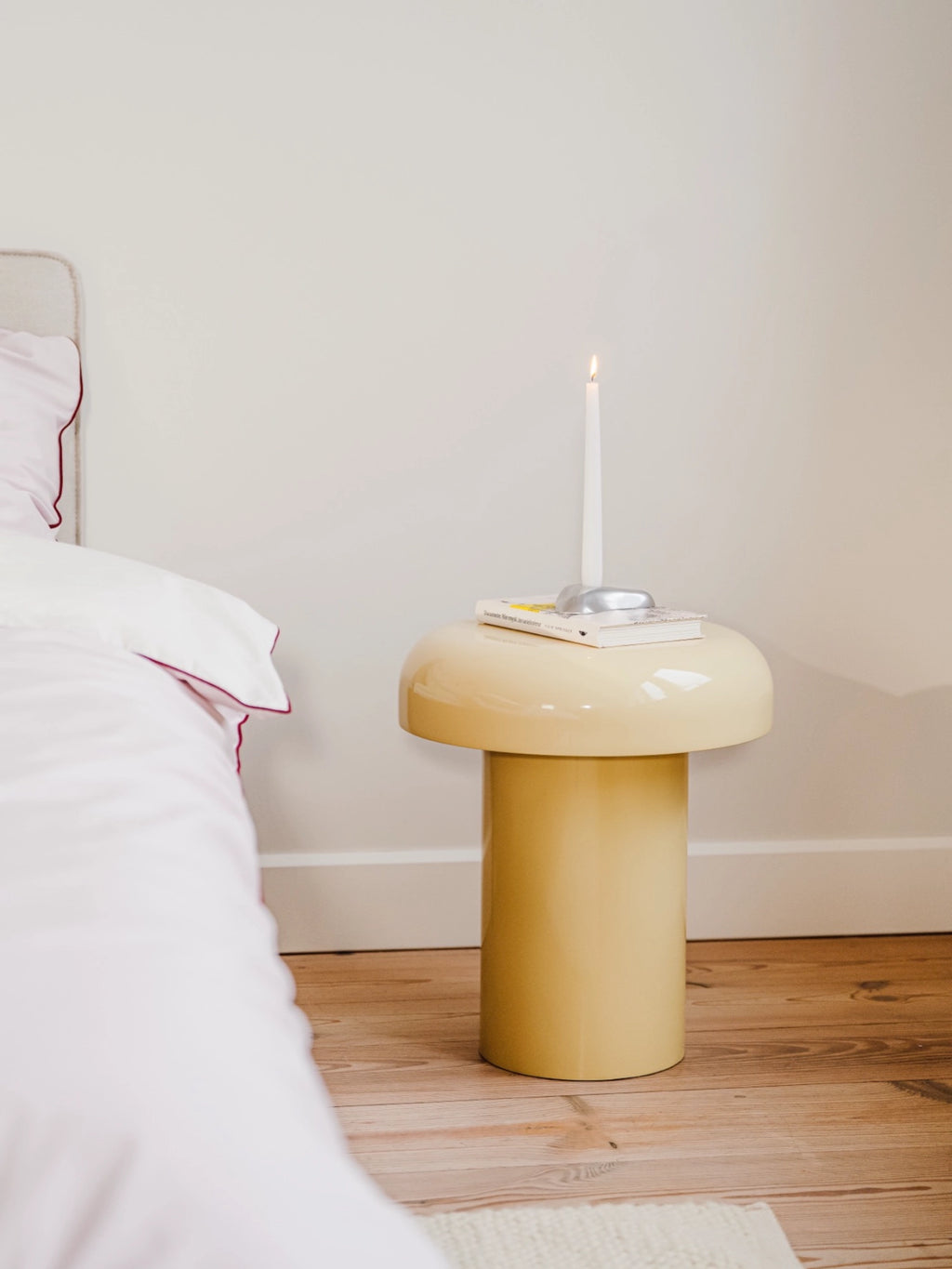 noo.ma Miko Side Table, a contemporary mushroom-shaped side table with a glossy pale yellow lacquered finish and a sculptural, organic silhouette. This modern accent table features a rounded top and a sturdy cylindrical base, evoking a playful 70s retro design aesthetic. Ideal as a stylish bedside table for a minimalist bedroom or a vibrant accent piece in a contemporary living room.