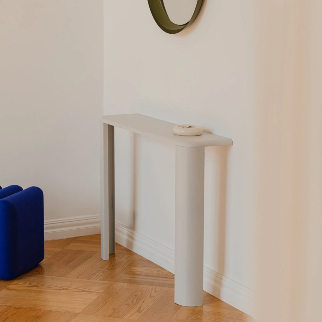 noo.ma Fli Console Table, a modern minimalist console table in a soft greige matte finish, featuring a slim rectangular top with gently rounded edges and distinctive U-shaped legs, one flat and one curved. This contemporary MDF entryway table offers an organic modern design, perfect for narrow hallways, living room accents, or Scandinavian-inspired spaces.