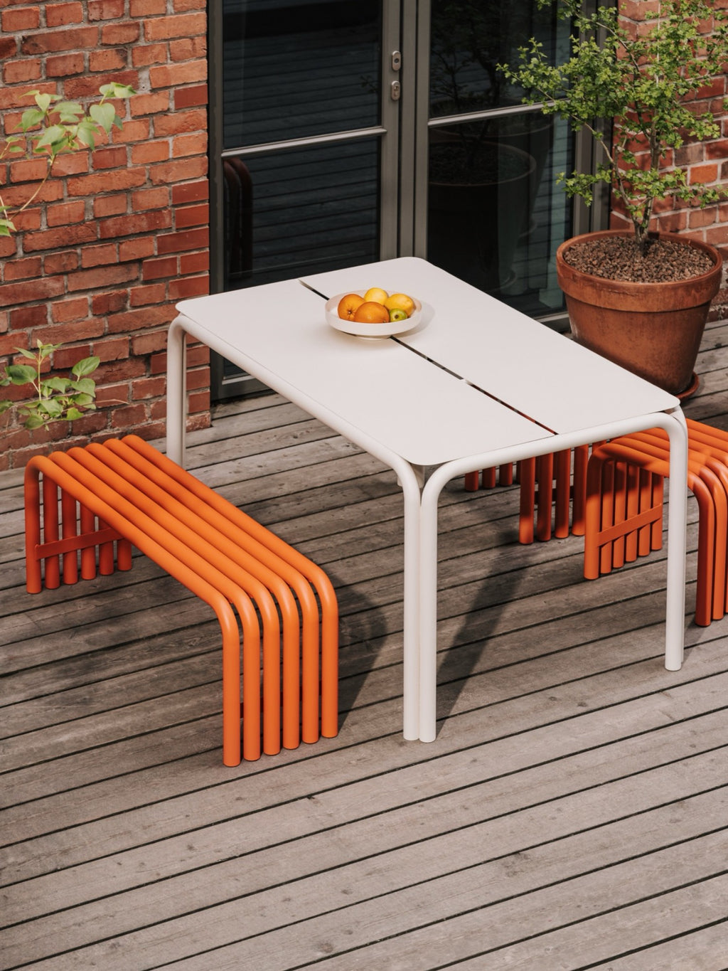 noo.ma Nokk Bench, a vibrant orange modern outdoor bench crafted from durable tubular powder-coated metal, featuring a distinctive curved, slatted seat design.