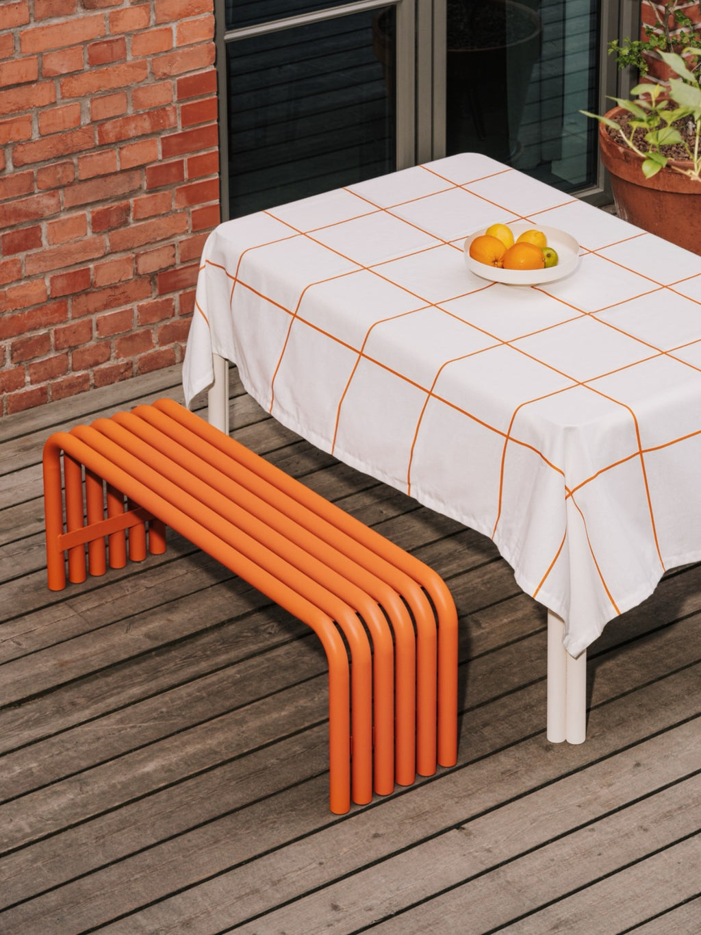 noo.ma Nokk Bench, a vibrant orange contemporary outdoor bench crafted from sturdy powder-coated tubular metal with a sleek, minimalist design. Its unique parallel bent tube construction forms a striking C-shape, offering durable and stylish seating for modern patios and garden spaces.