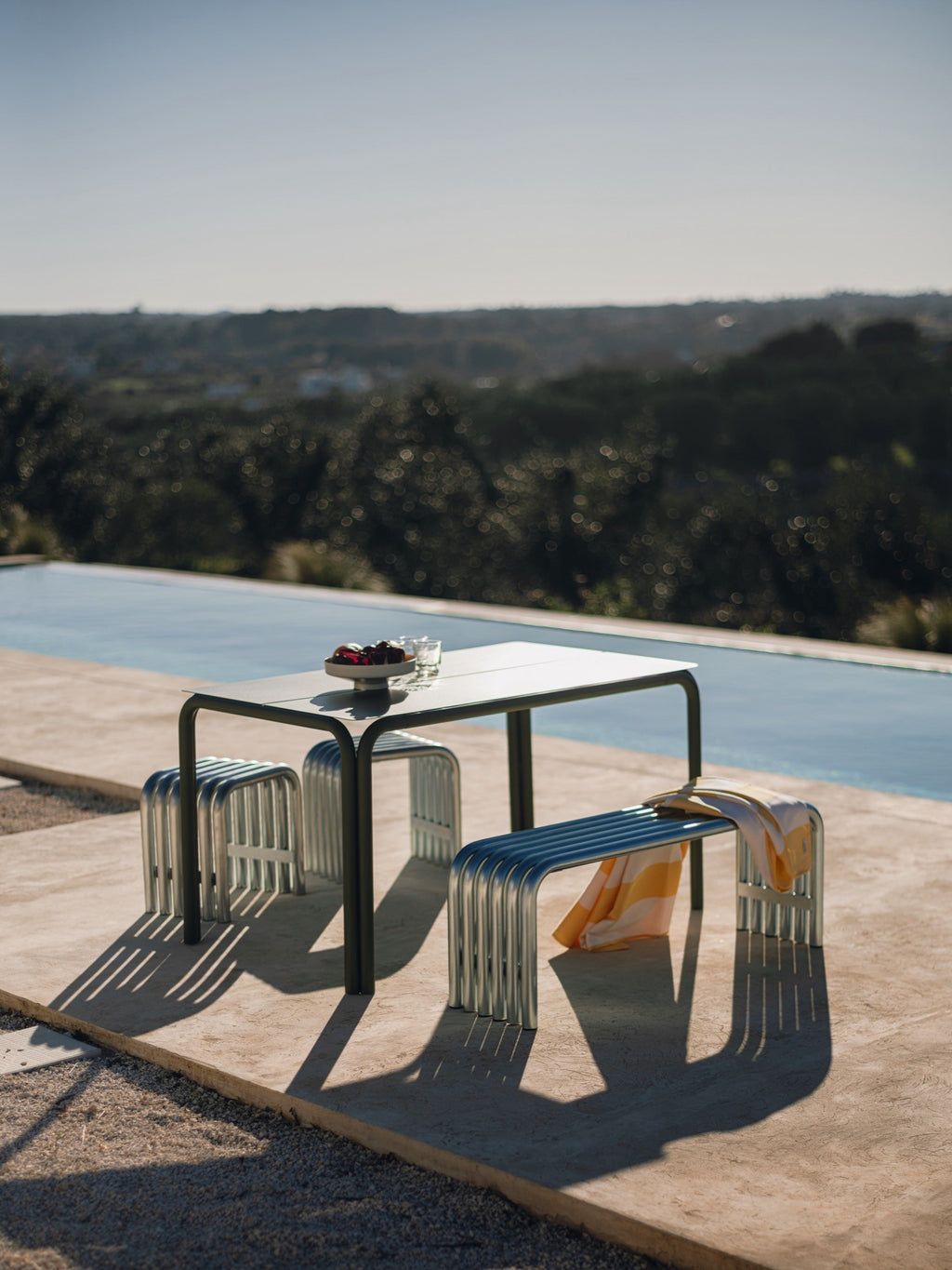 noo.ma Nokk Bench, a modern minimalist outdoor bench featuring a striking tubular design in polished silver metal with a ribbed texture and sleek, curved lines.