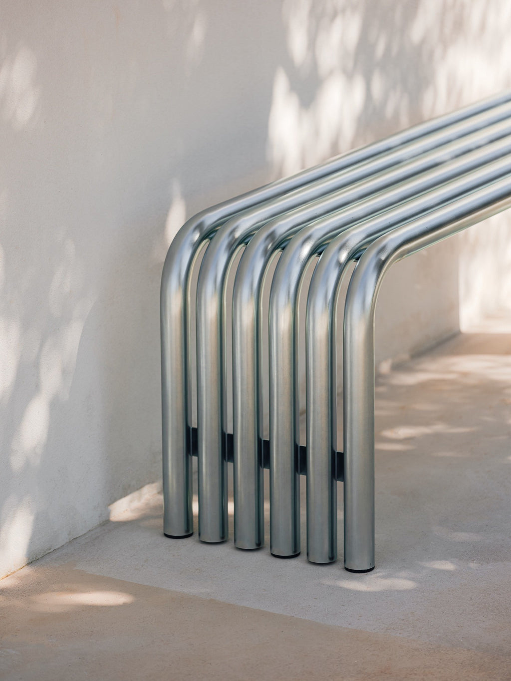 noo.ma Nokk Bench, a modern minimalist outdoor bench crafted from multiple parallel bent matte silver metal tubes, forming a clean, industrial-chic silhouette. This contemporary metal tube bench offers sleek public seating or stylish garden furniture for urban patios and minimalist landscape designs.